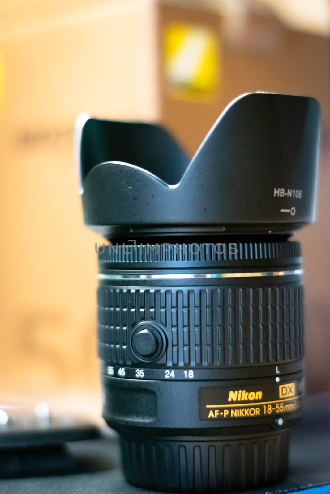 Nikon kit lens 18-55mm with a lens hood on it and it's box behind in the background.