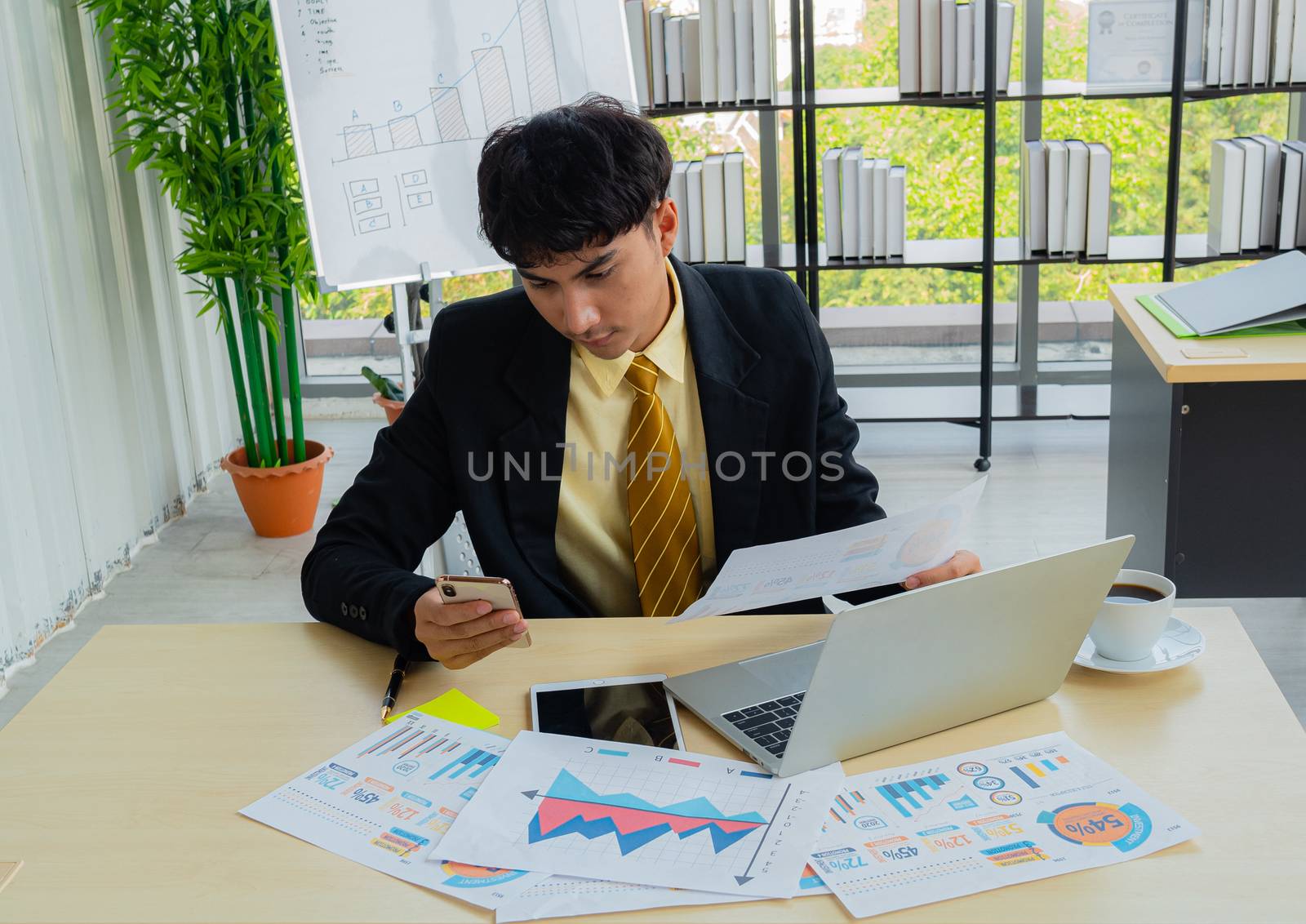 Young business people are concentrating on their work by comparing the results of their mobile phones with hand-held documents on the office desk full of information in the modern office.