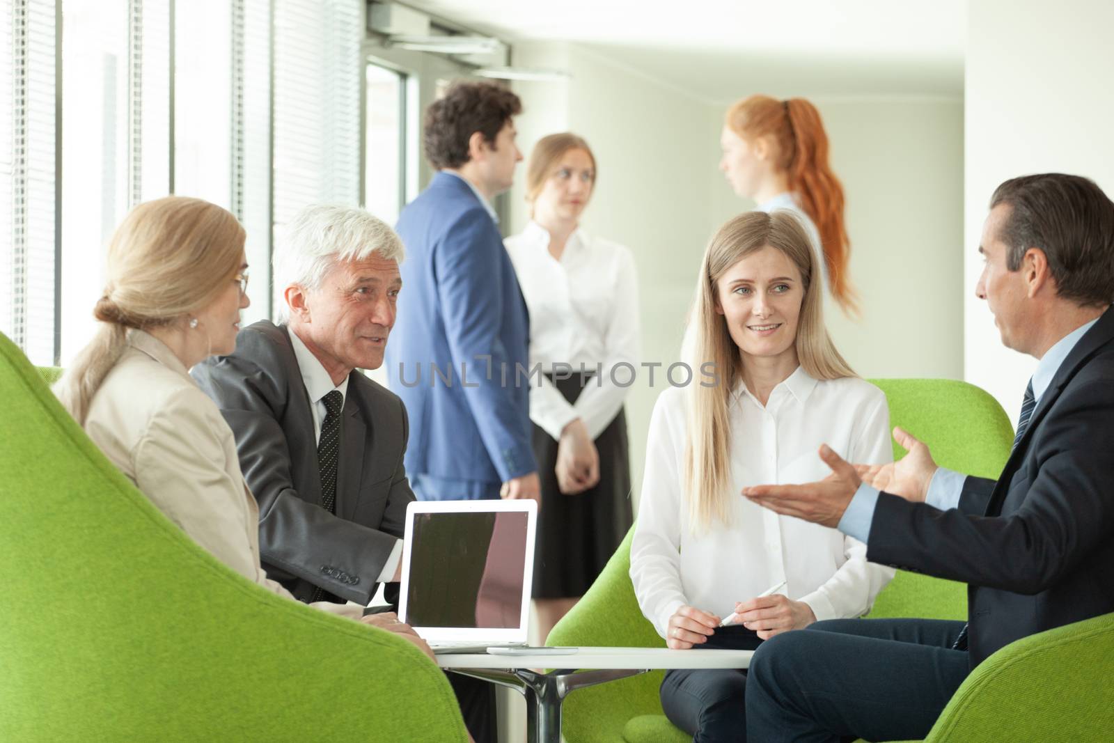 Business people sitting together on armchairs in office hall and having a negotiation discussion