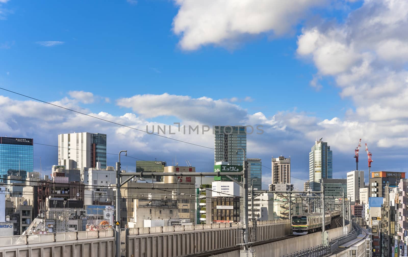 kanda station where the trains of the yamanote line pass between the top of the buildings of the district of Chiyoda under the blue sky of Tokyo.