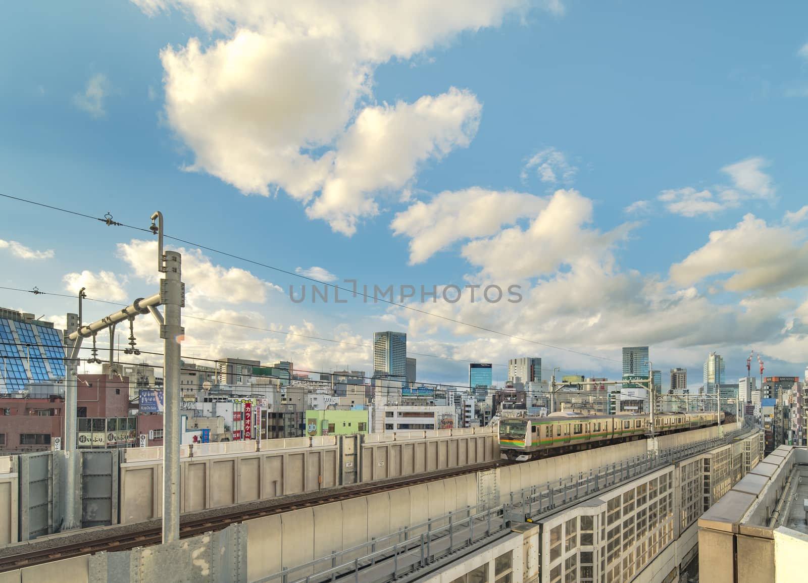 kanda station where the trains of the yamanote line pass between the top of the buildings of the district of Chiyoda under the blue sky of Tokyo.