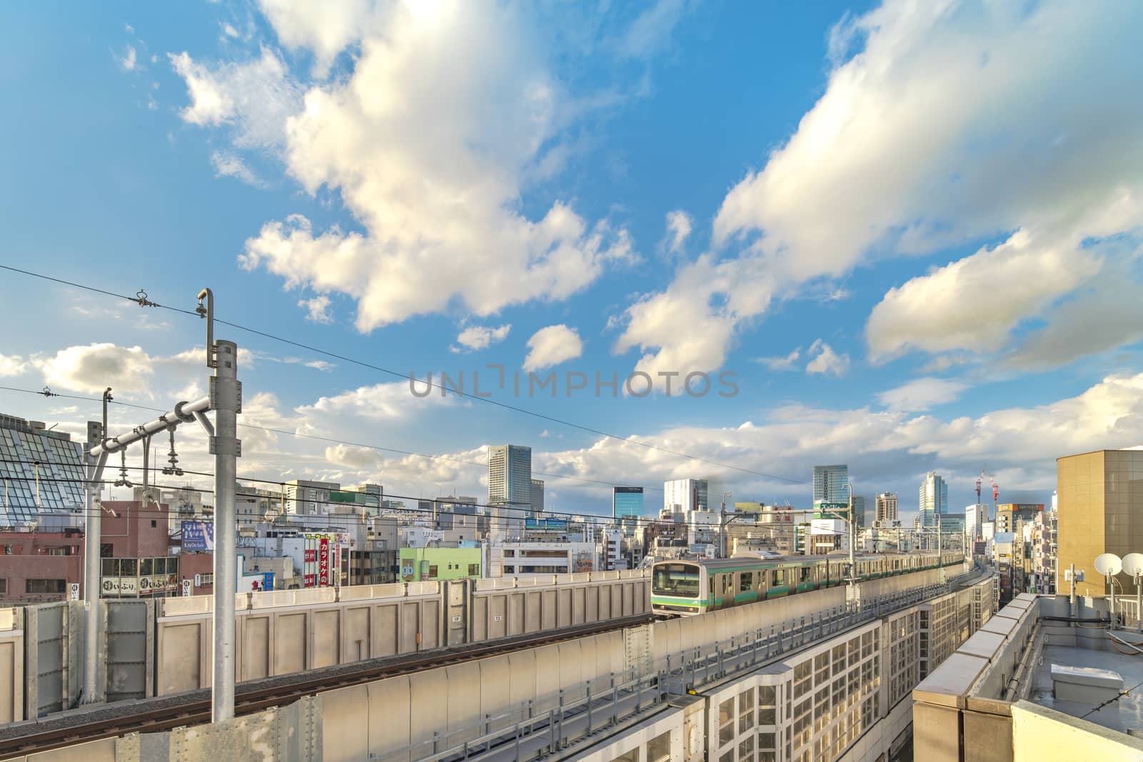 kanda station where the trains of the yamanote line pass between the top of the buildings of the district of Chiyoda under the blue sky of Tokyo.