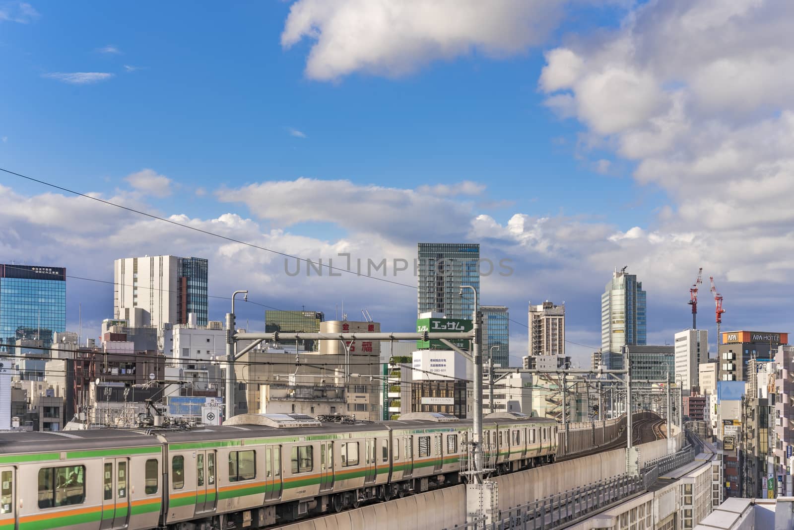 kanda station where the trains of the yamanote line pass between the top of the buildings of the district of Chiyoda under the blue sky of Tokyo.