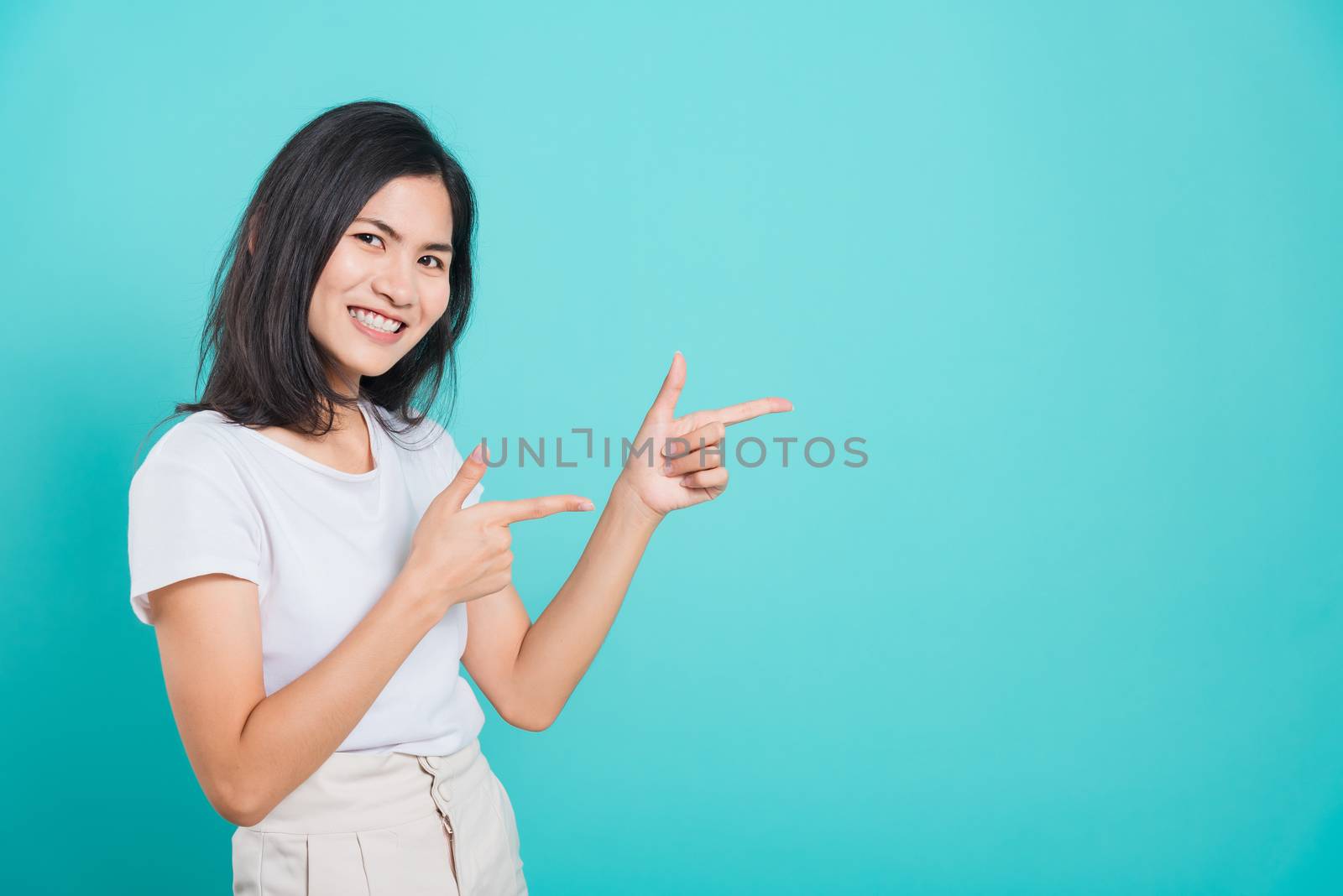 Portrait Asian beautiful young woman wearing white T-shirt standing smile white teeth, She pointing finger up and looking at camera, shoot photo in studio on blue background, There was copy space.