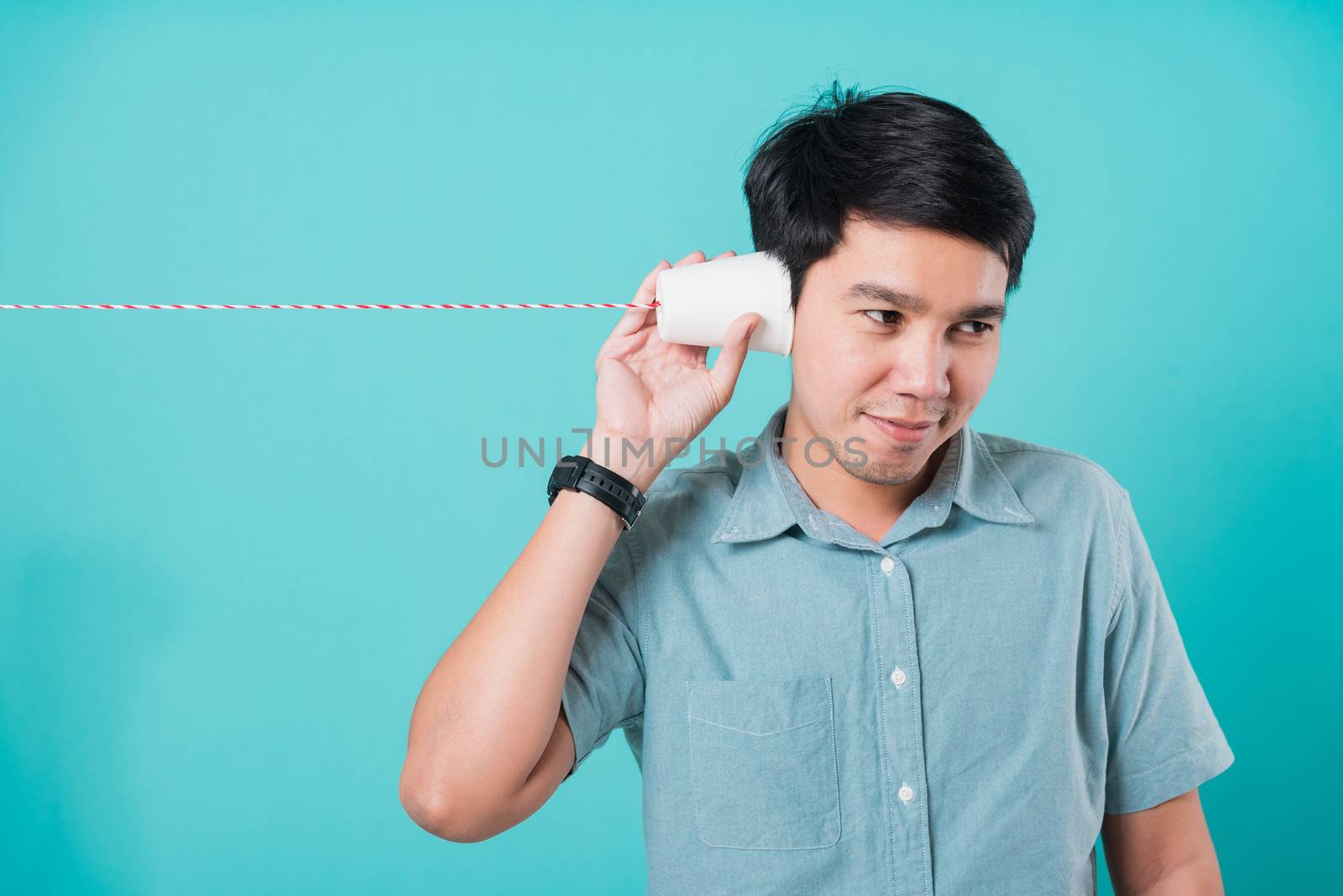 Portrait happy Asian handsome young man smile white teeth standing wear shirt, He holding paper can telephone for listening the message, studio shot on blue background