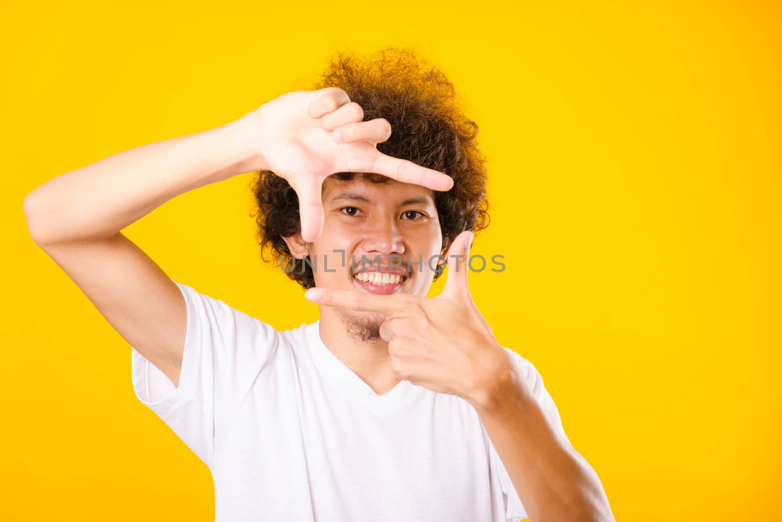 Asian handsome man with curly hair he smiling making frame with hands and fingers with happy face for creativity photography isolate on yellow background