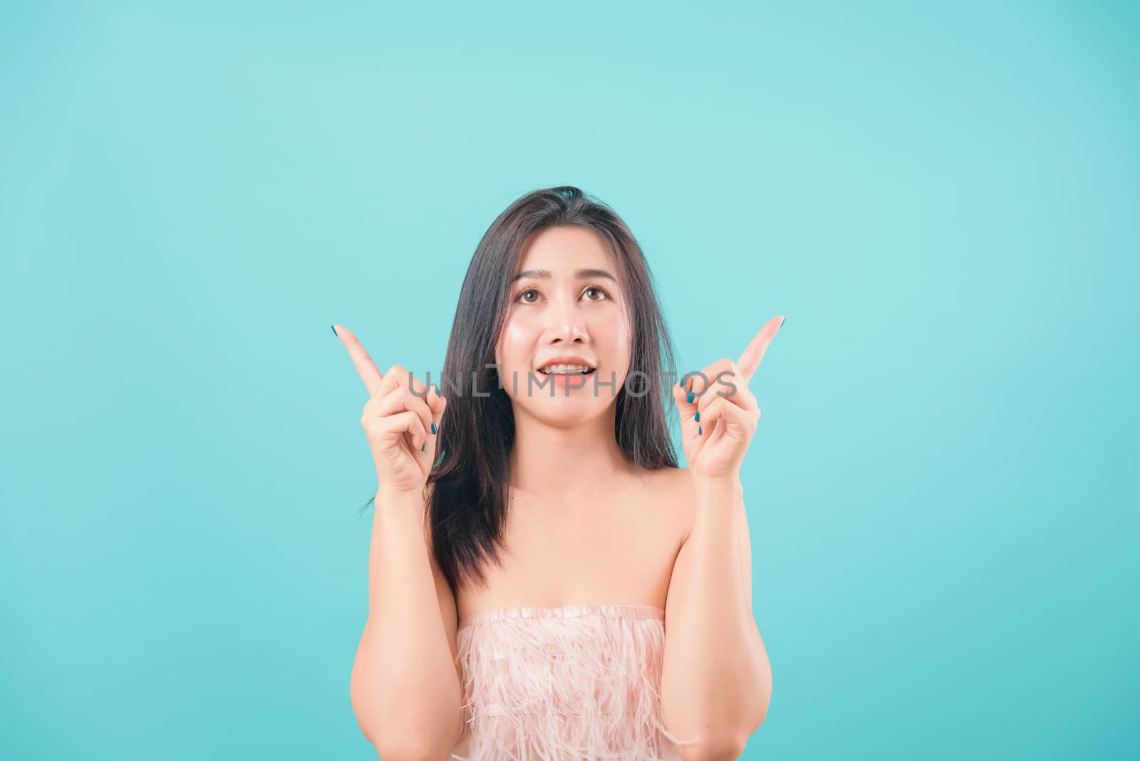 Asian happy portrait beautiful young woman standing her pointer finger up isolated on blue background with copy space for text