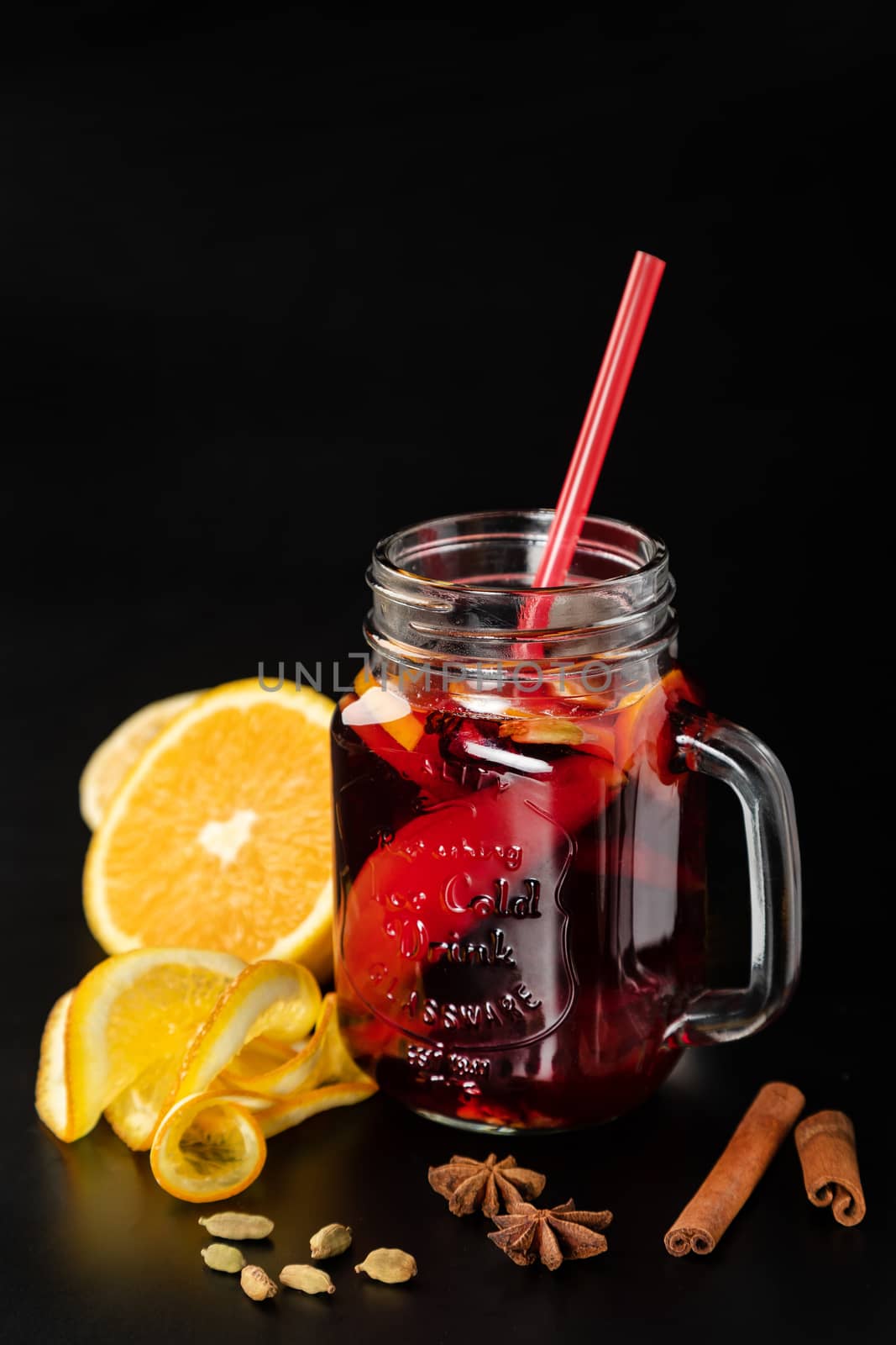 Mulled wine in a glass mug with fruits and spices on a plain black background