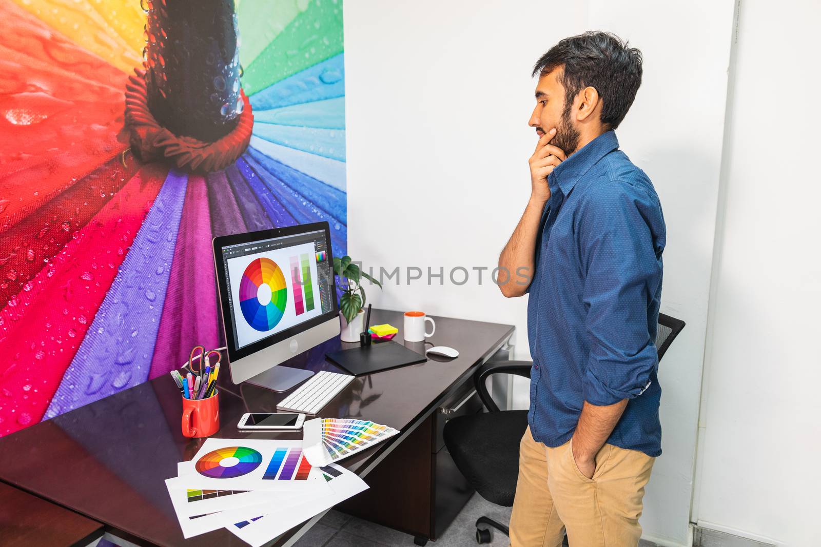 Young bearded man standing and looking at the computer by bmphotographypty