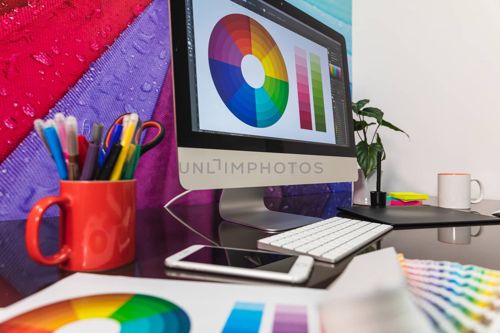 Modern graphic designer office workplace with digital tablet, notepad, colorful pencils, cellphone. Some Color swatch samples over modern desk