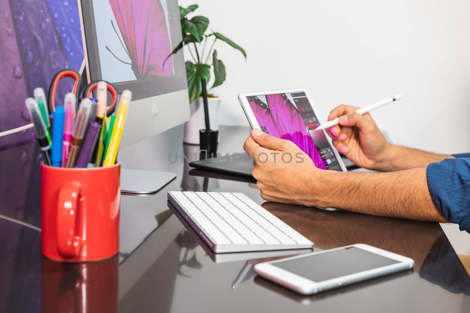 Close Up view. Man sitting in office at table with stationary and is using a tablet. Man Drawing