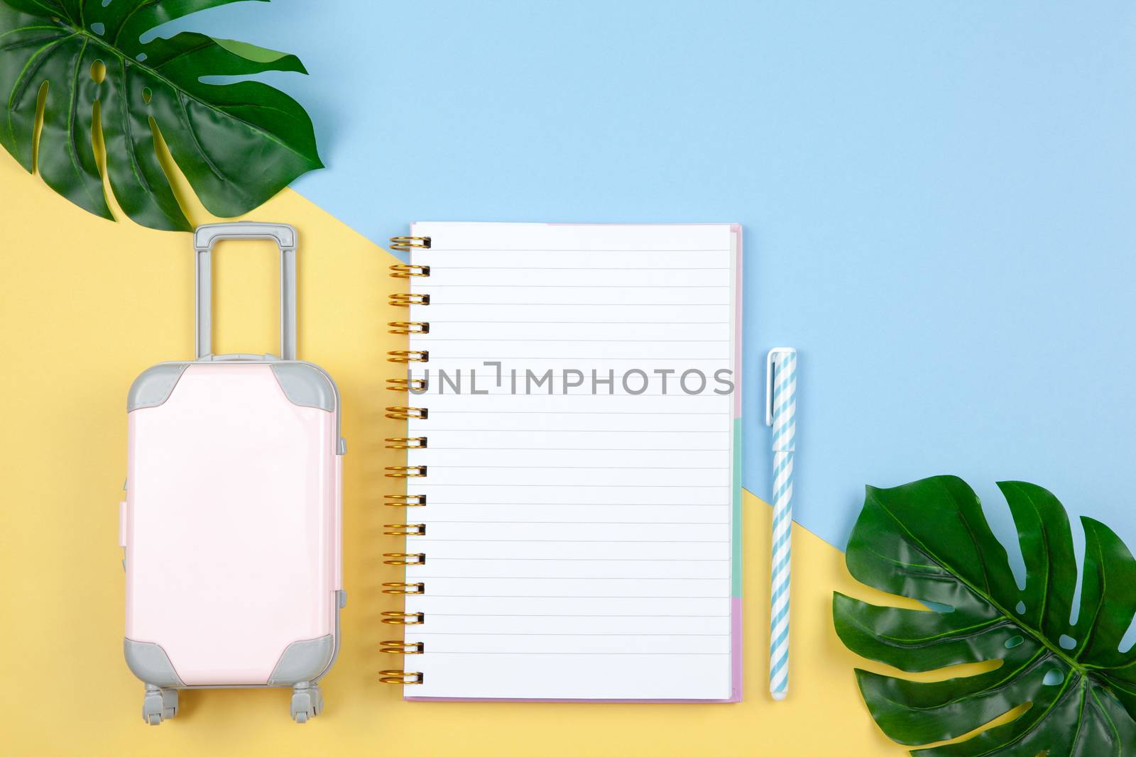 Notebook, pen, suitcase, monstera leaves on yellow and blue background, copy space, flat lay. For lifestyle blog, social media. Freelance, planning of vacation, travel, sales concept. Horizontal by ALLUNEED