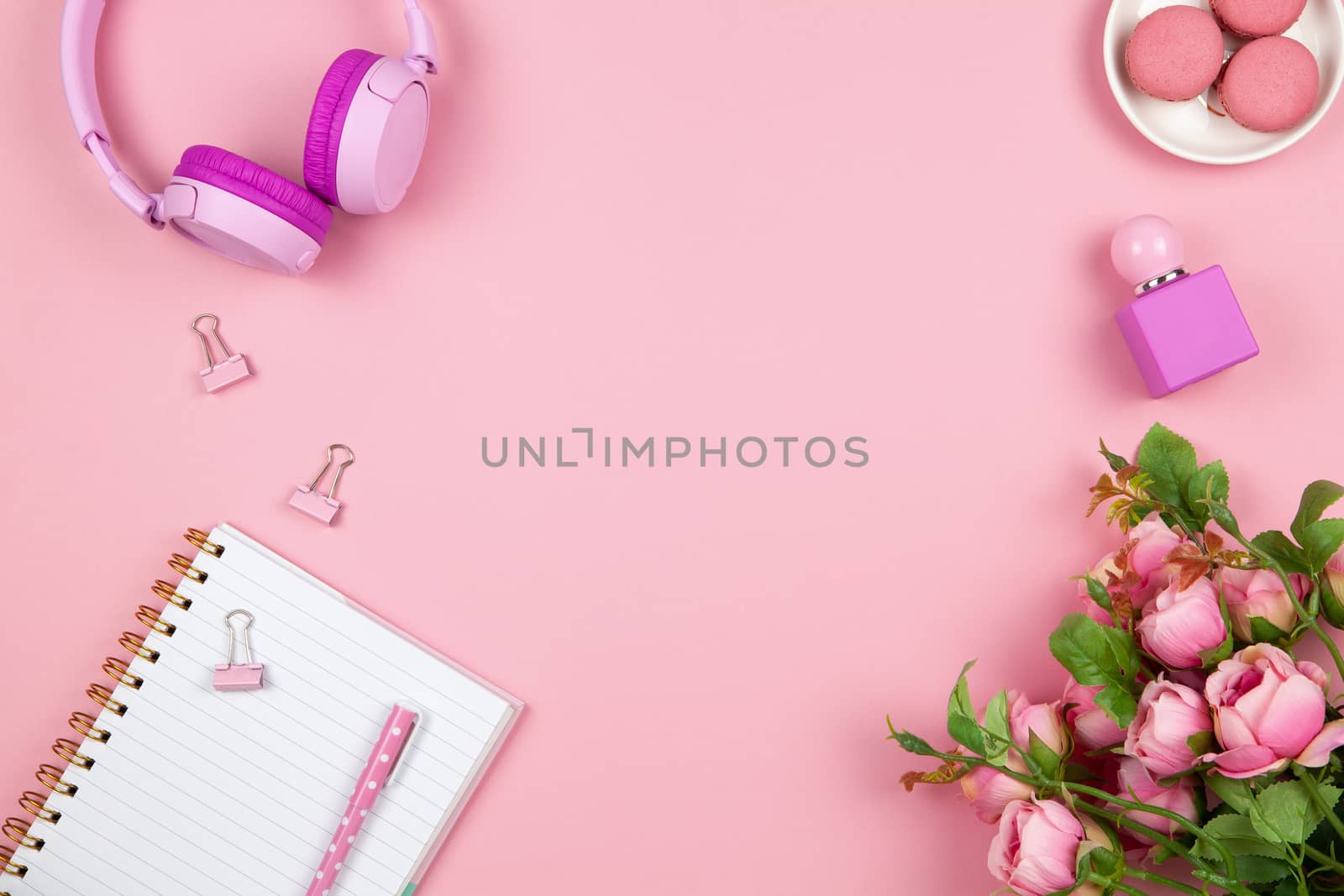 Modern female working space, top view. Women's or girls things, wireless headphones, roses, perfume, stationery on pink backround, copy space, flat lay. Work from home concept. For blog. Horizontal.
