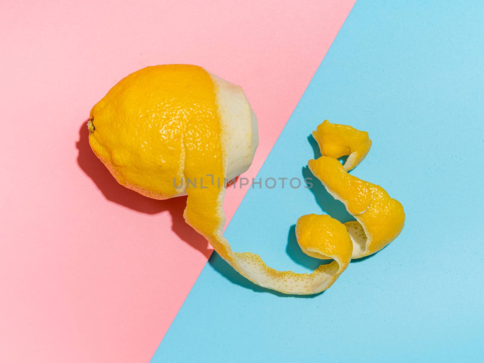Lemon with spiral peeled zest over blue and pink minimalistic background. Lemon and peel in hard light. Top view or flat lay. Summer minimalistic creative concept and layout