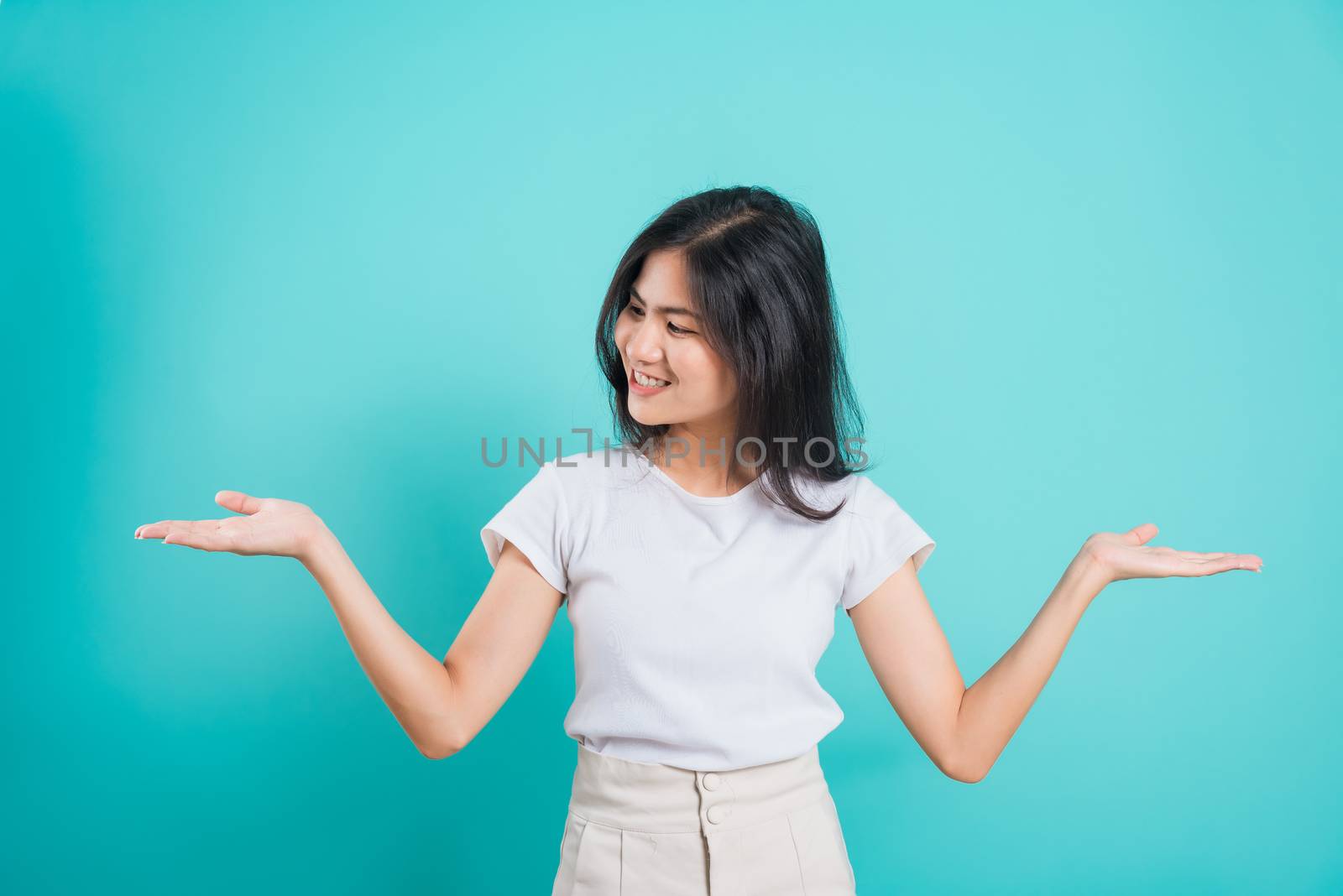 Portrait Asian beautiful young woman standing wear t-shirt, She showing hand to presenting product and looking to product, shoot photo in a studio on blue background, There was copy space