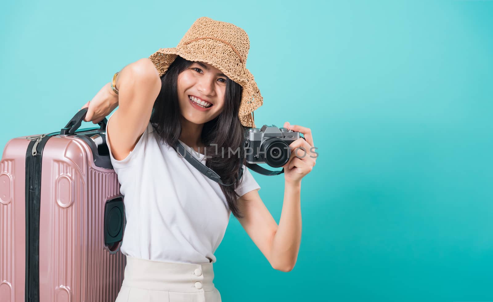 Traveler tourist happy Asian beautiful young woman standing wear white t-shirt, holidays travel concept, her holding suitcase bag and photo mirrorless camera, shoot photo in studio on blue background