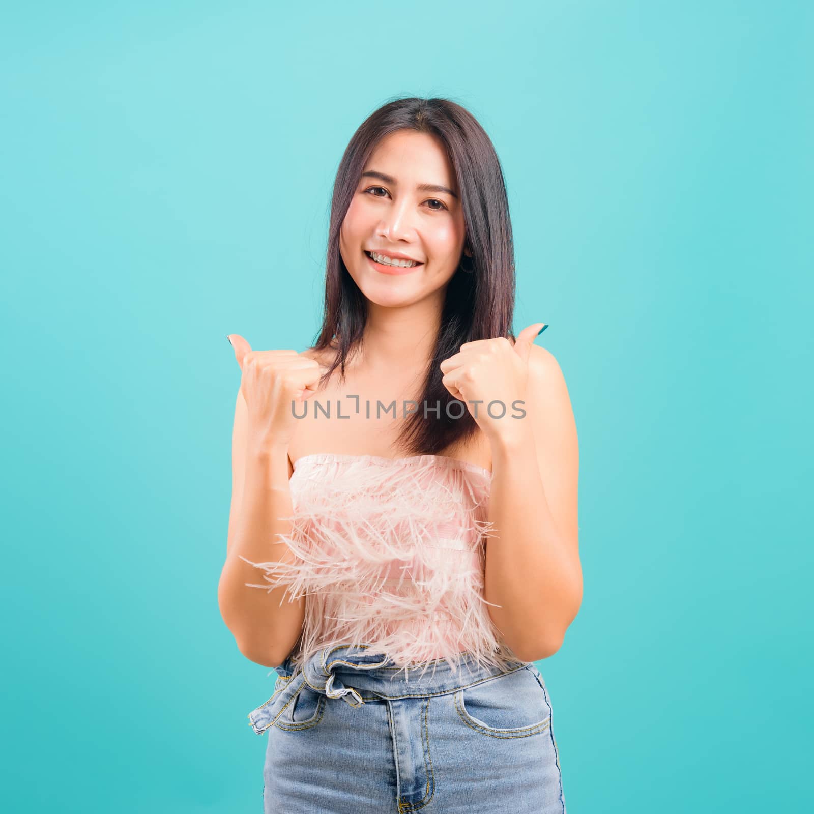 Portrait asian beautiful woman smiling showing hand showing thumbs up sign and her looking to camera on blue background, with copy space for text