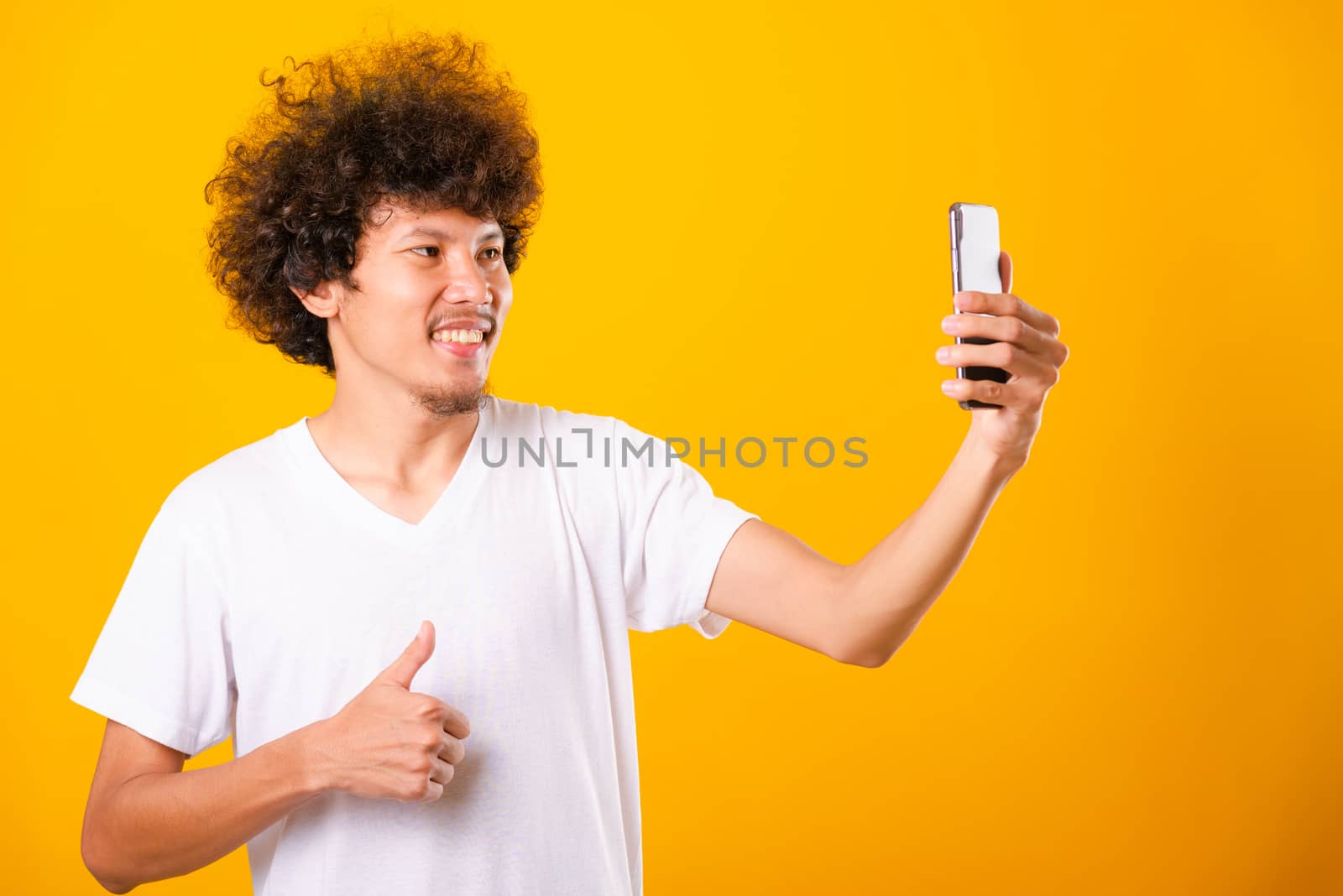 Portrait asian handsome man curly hair taking selfie with mobile phone isolated on yellow background