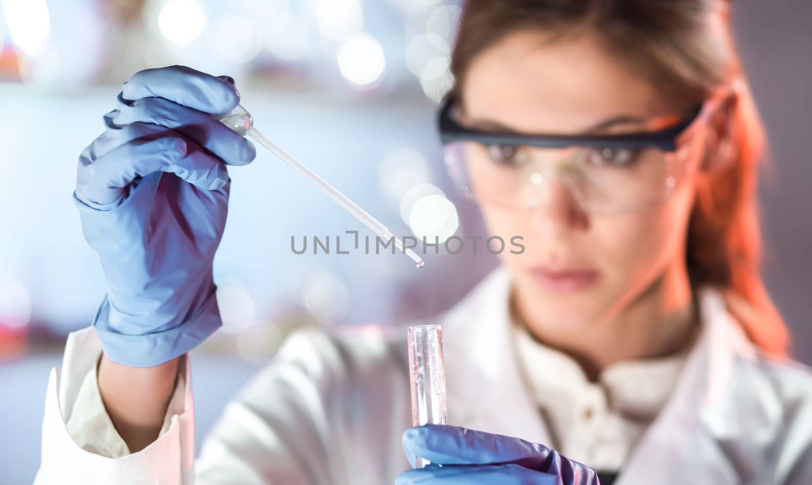 Life scientists researching in laboratory. Focused female life science professional pipetting solution into the glass cuvette. Lens focus on researcher's eyes. Healthcare and biotechnology concept.