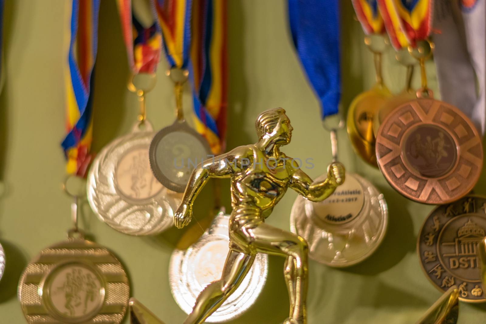 A gold trophy symbolizing an athlete running and many medals in the background, Bucharest, Romania