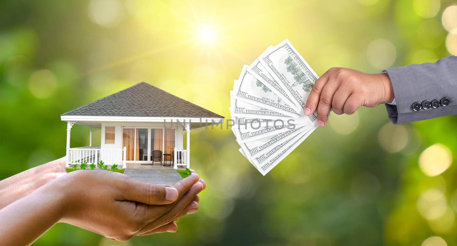 The hands of a businessman hold money and the other hand holds a house. The idea of saving money to buy a house