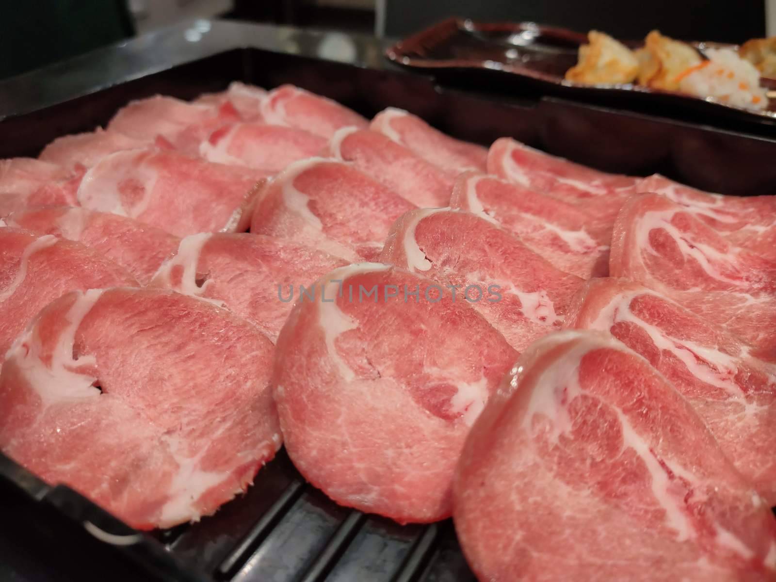 Fresh pork sliced for japanese hot pot on black plate by peerapixs