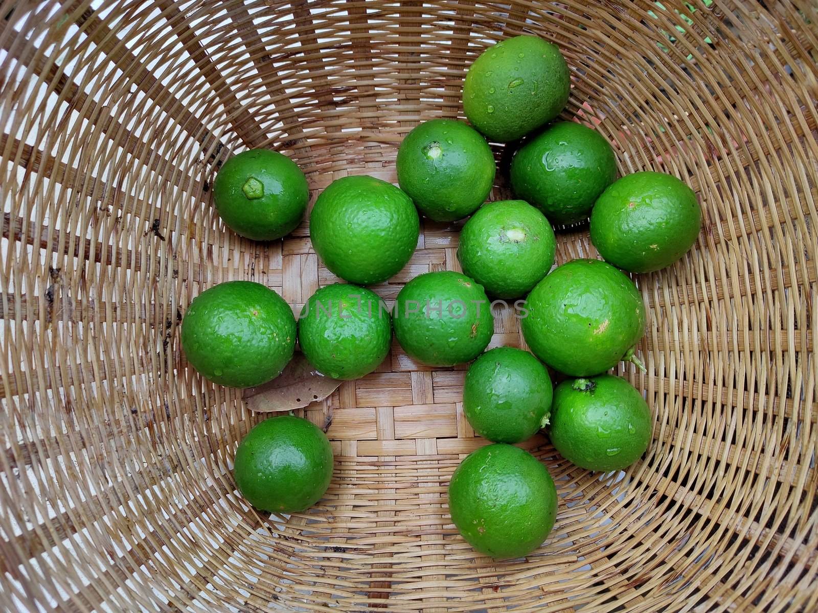 Fresh green limes in the small colorful baskets on the woven bamboo plate. The Thai traditional fresh market. by peerapixs