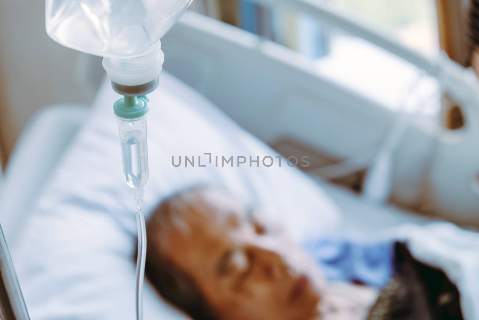 Elderly patients in hospital bed background, Close up of IV saline solution drip