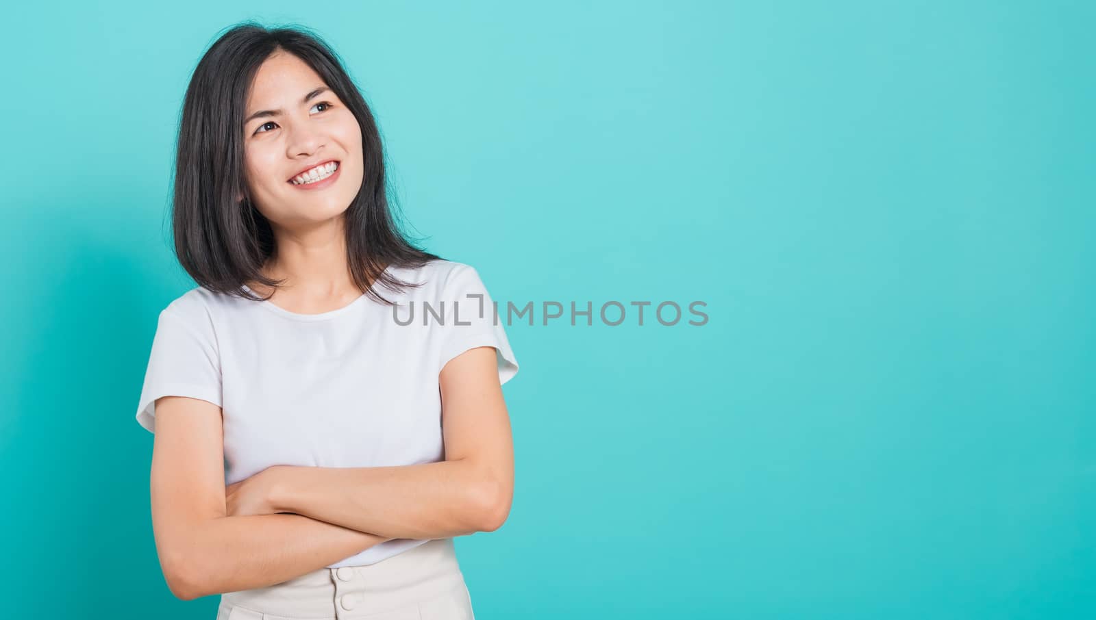 Portrait Asian beautiful happy young woman smile wear white t-shirt standing with a chest looking up away at copy space, on a blue background