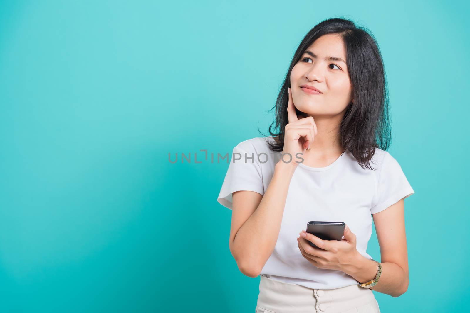 Portrait Asian beautiful happy young woman standing smile, posing using mobile phone her thinking dreaming on blue background, with copyspace