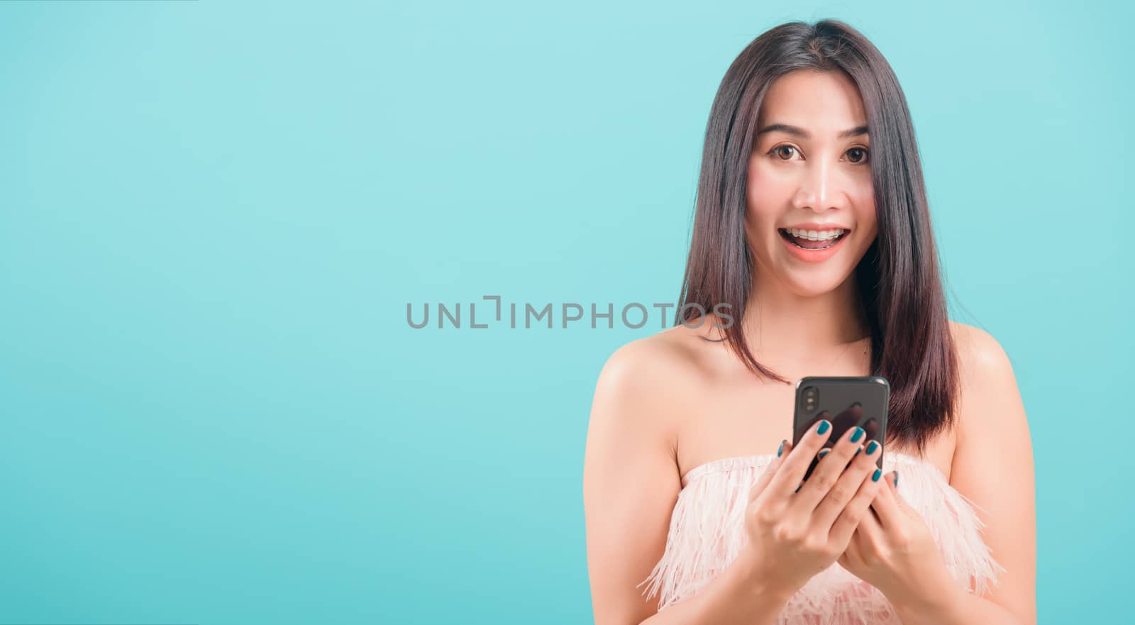 Asian happy portrait beautiful young woman standing smile her  holding smartphone or mobile phone and looking to camera on blue background with copy space for text