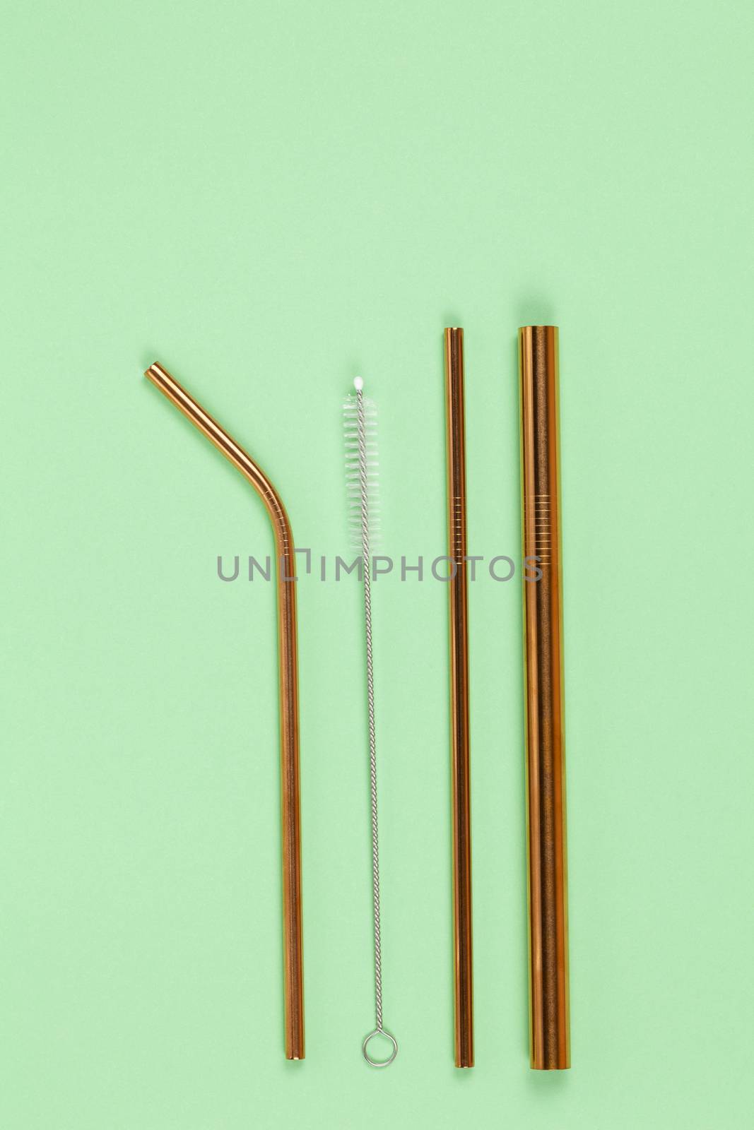 Tubes from environmental reusable metal opposition to plastic disposable tubes on green background. Alternative to disposable tableware, zero waste concept. Vertical. Flat lay, close-up, top veiw.