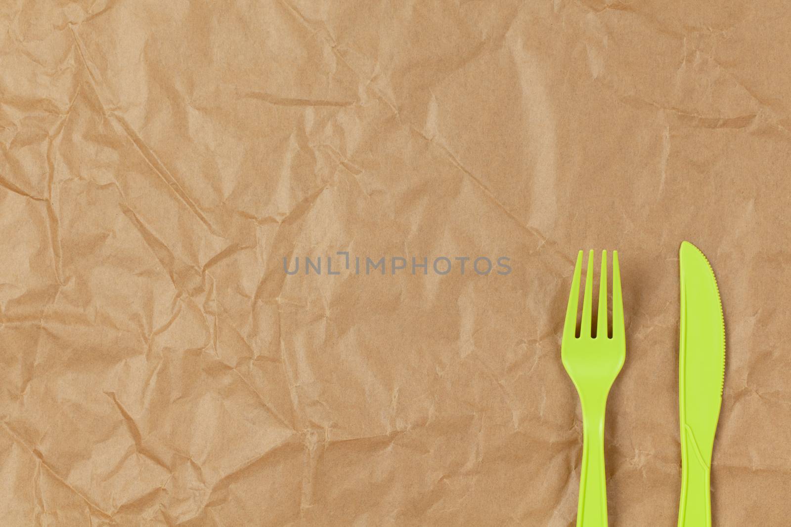 Reusable recyclable green fork, knife made from corn starch on brown crumpled craft paper, copy space. Eco, zero waste, alternative to plastic concept. Flat lay. Horizontal. Close-up by ALLUNEED