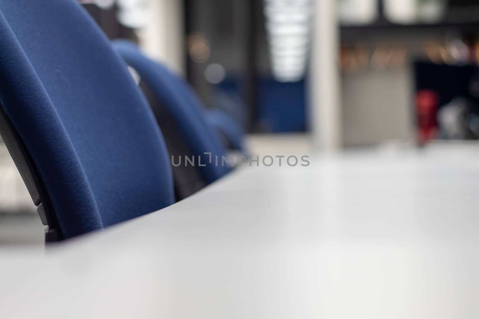 Chairs are lined up at a long desk in a co-working office space. The chairs are seen from the level of the desk and fade into a blurry background with that surface.