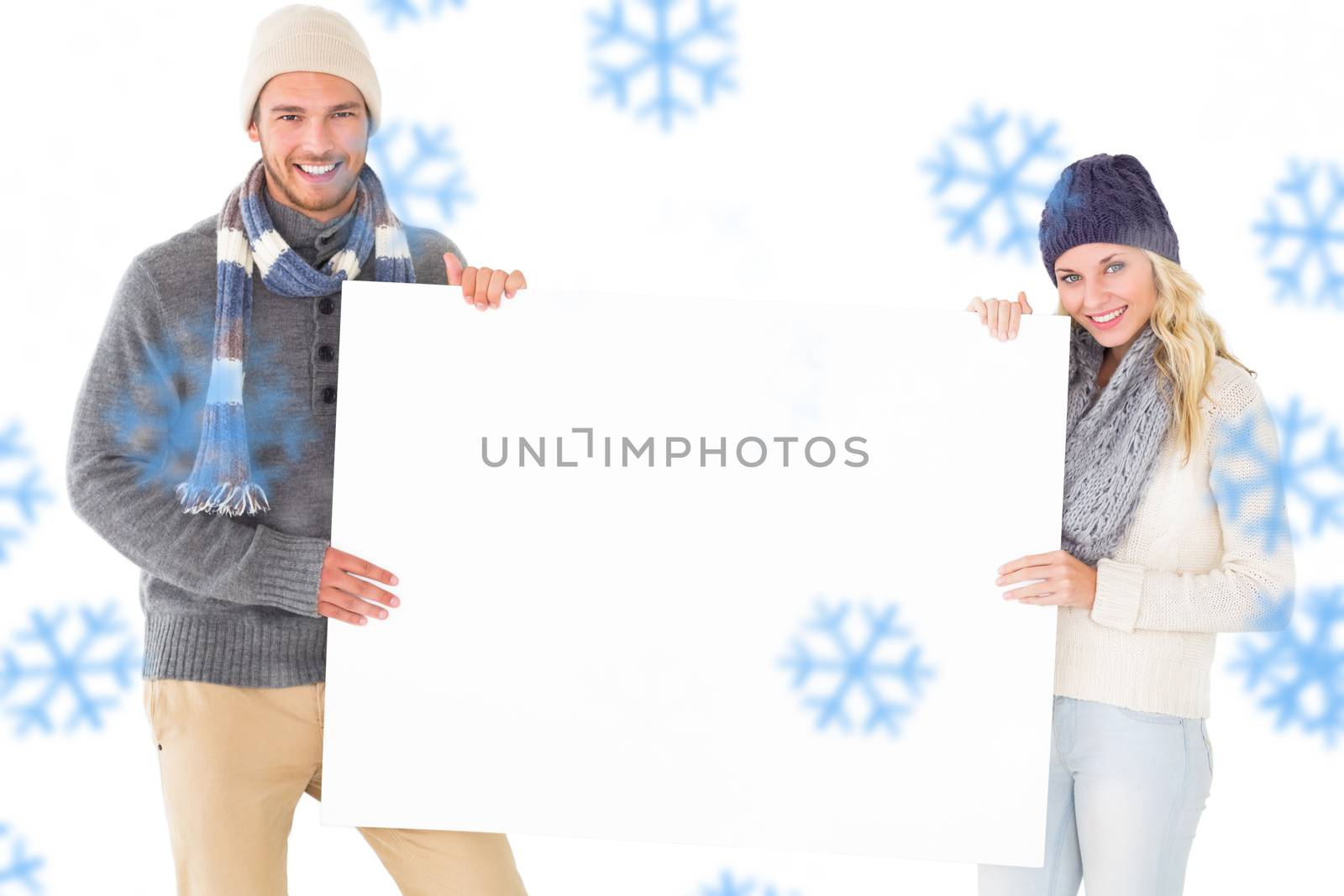 Attractive couple in winter fashion showing poster against snowflakes