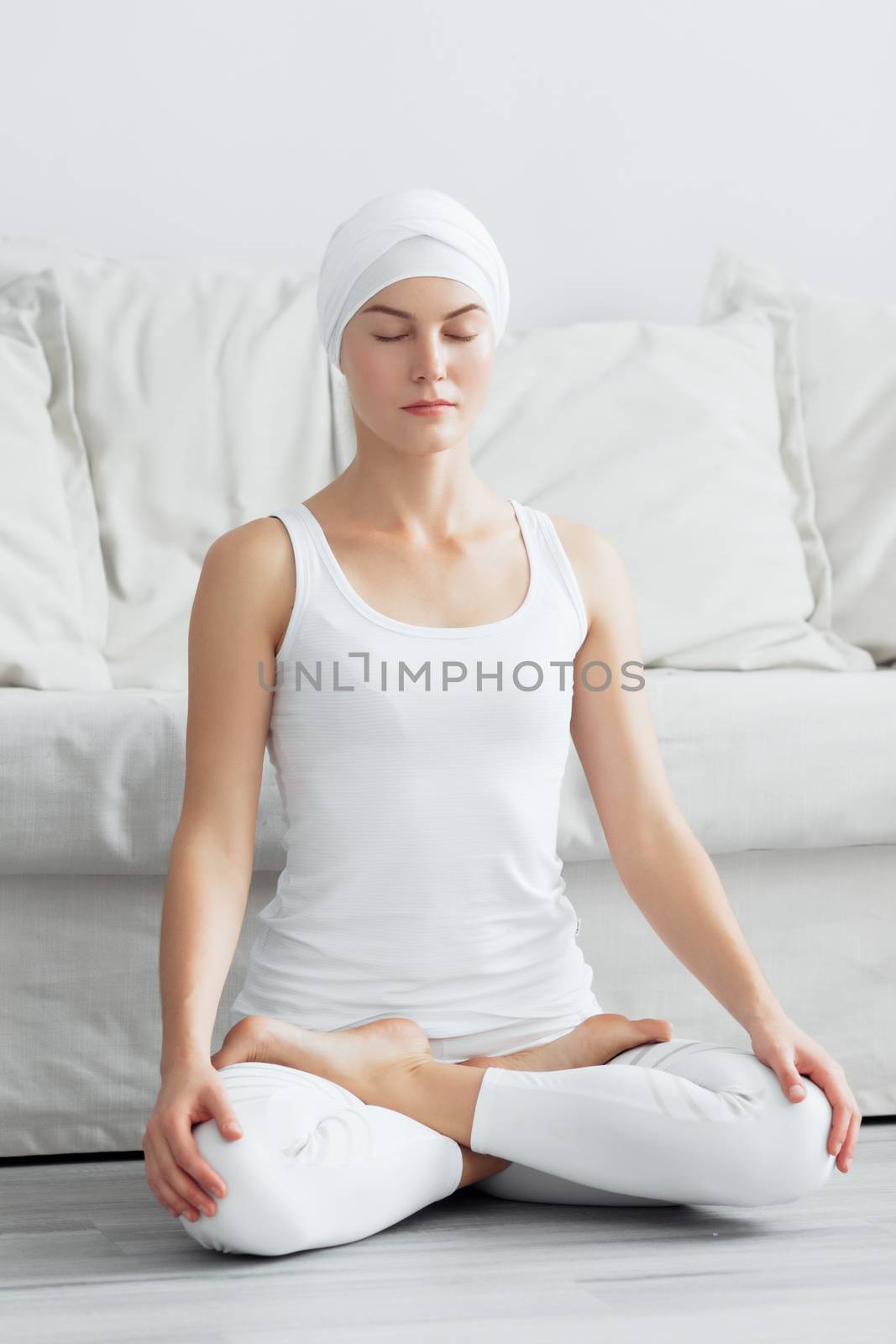 Pretty young woman in sportswear sitting on studio floor in difficult position while doing yoga
