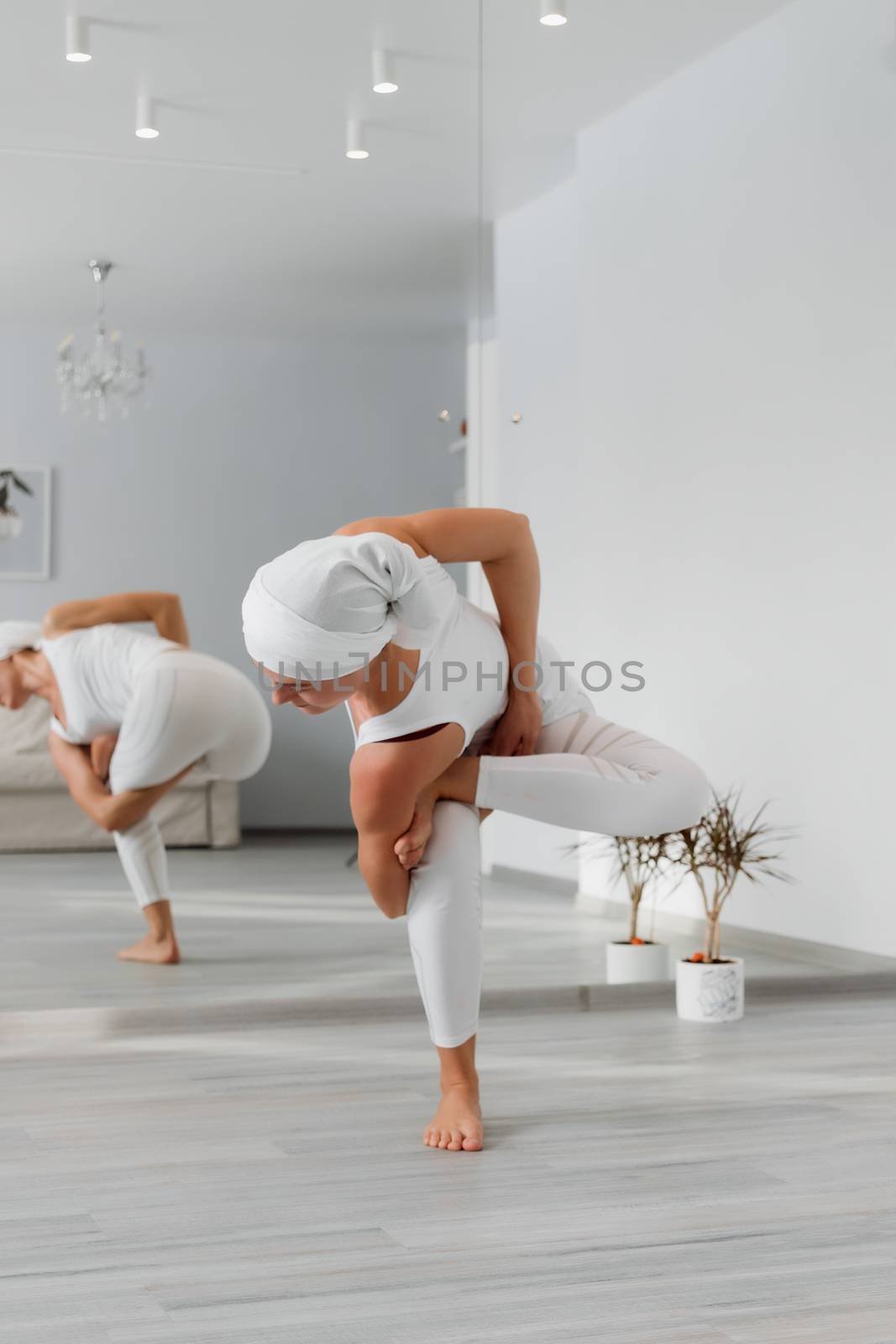 Pretty young woman in sportswear sitting on studio floor in difficult position while doing yoga
