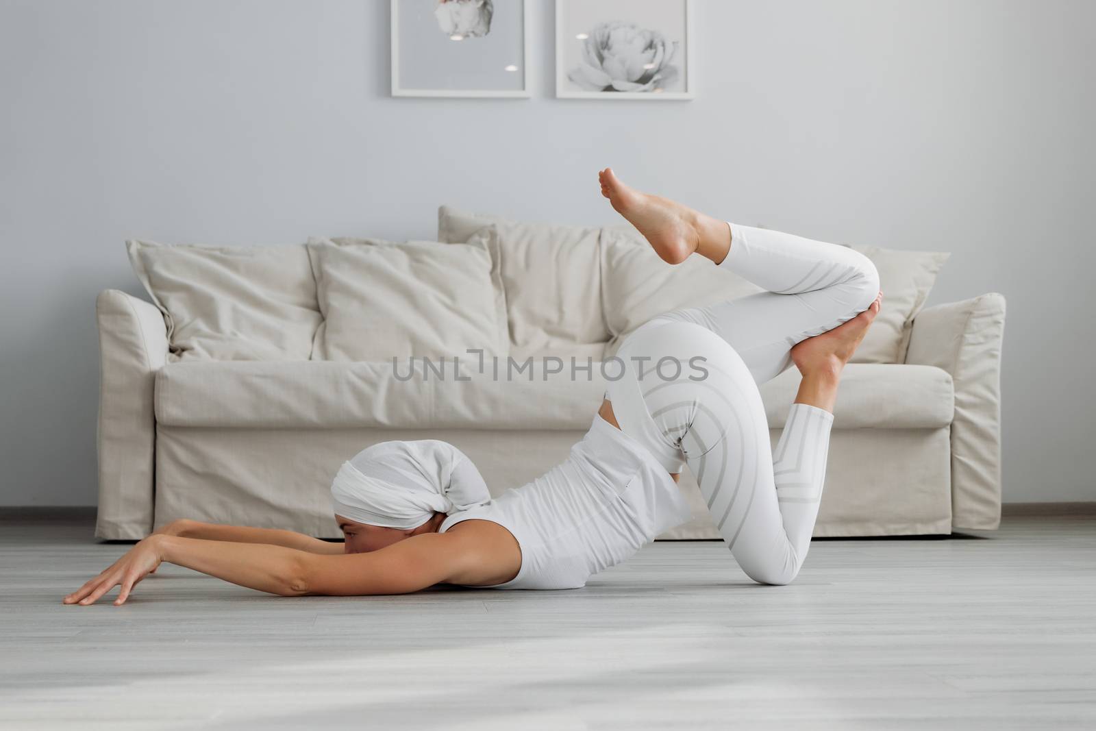 Pretty young woman in sportswear sitting on studio floor in difficult position while doing yoga