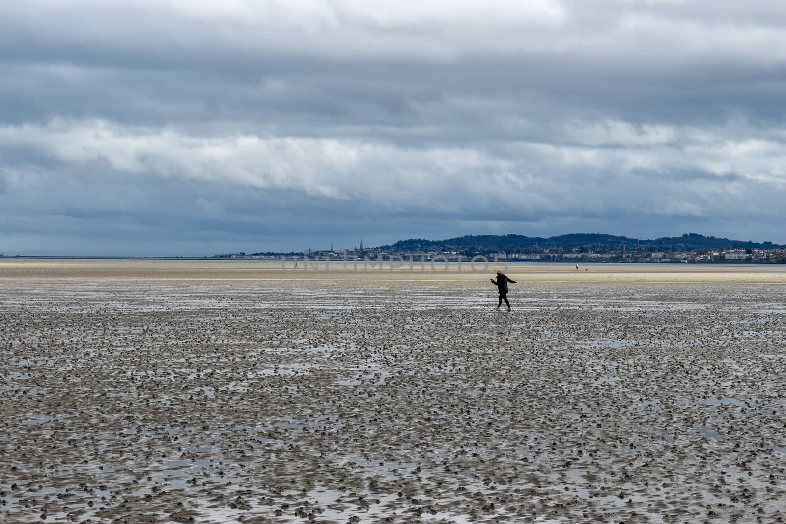 A woman maintaining social distancing walking outdoors on the beach in Dublin, Ireland by benentaylor