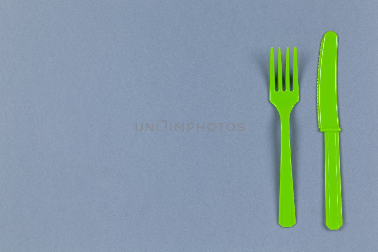 Reusable recyclable green fork, knife made from corn starch on grey background, copy space. Eco, zero waste, alternative to plastic concept. Flat lay, top view. Horizontal. Close-up.
