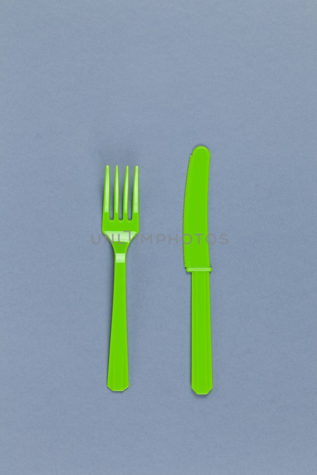 Reusable recyclable green fork, knife made from corn starch on grey background. Eco, zero waste, alternative to plastic concept. Flat lay, top view. Vertical. Close-up by ALLUNEED