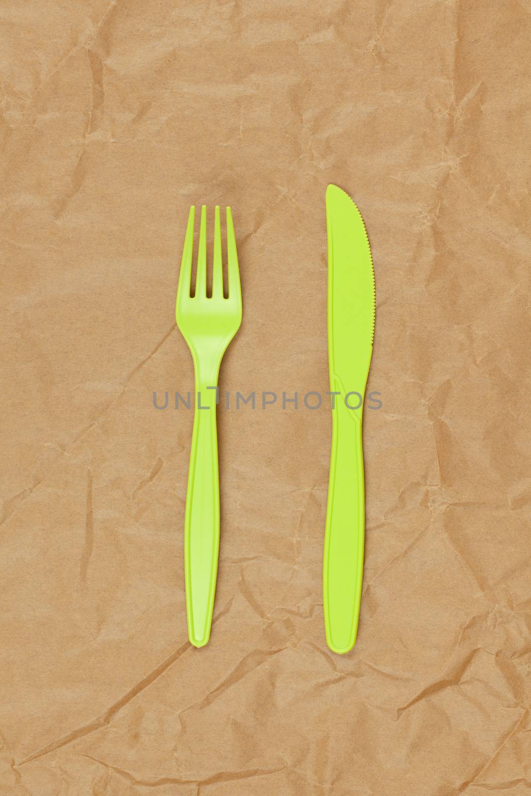 Reusable recyclable green fork, knife made from corn starch on brown crumpled craft paper, copy space. Eco, zero waste, alternative to plastic concept. Flat lay. Vertical. Close-up.