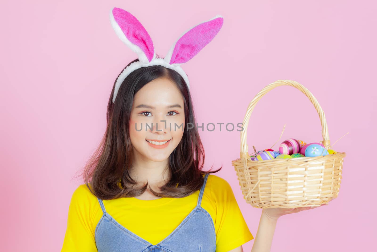 Portrait of a happy young woman wearing Easter bunny ears prepares to celebrate Easter on a pink background.