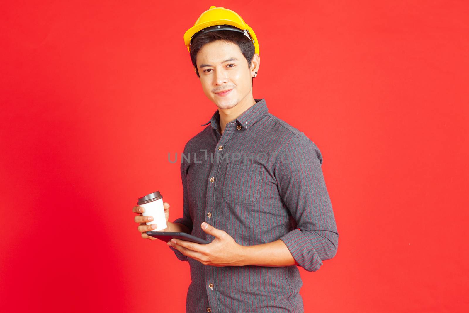 A portrait of a young engineer standing on a red background smiling and enjoying the taste of coffee during the lunch break.