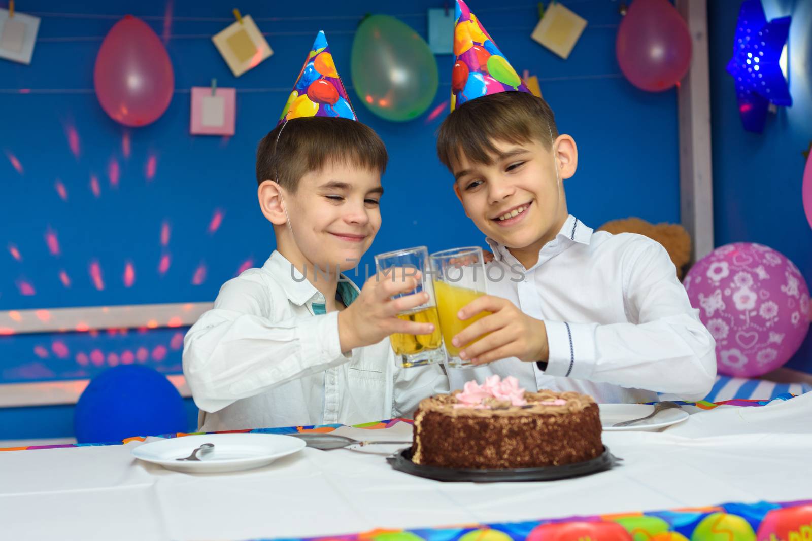 Two brothers banging glasses of juice at a birthday party by Madhourse