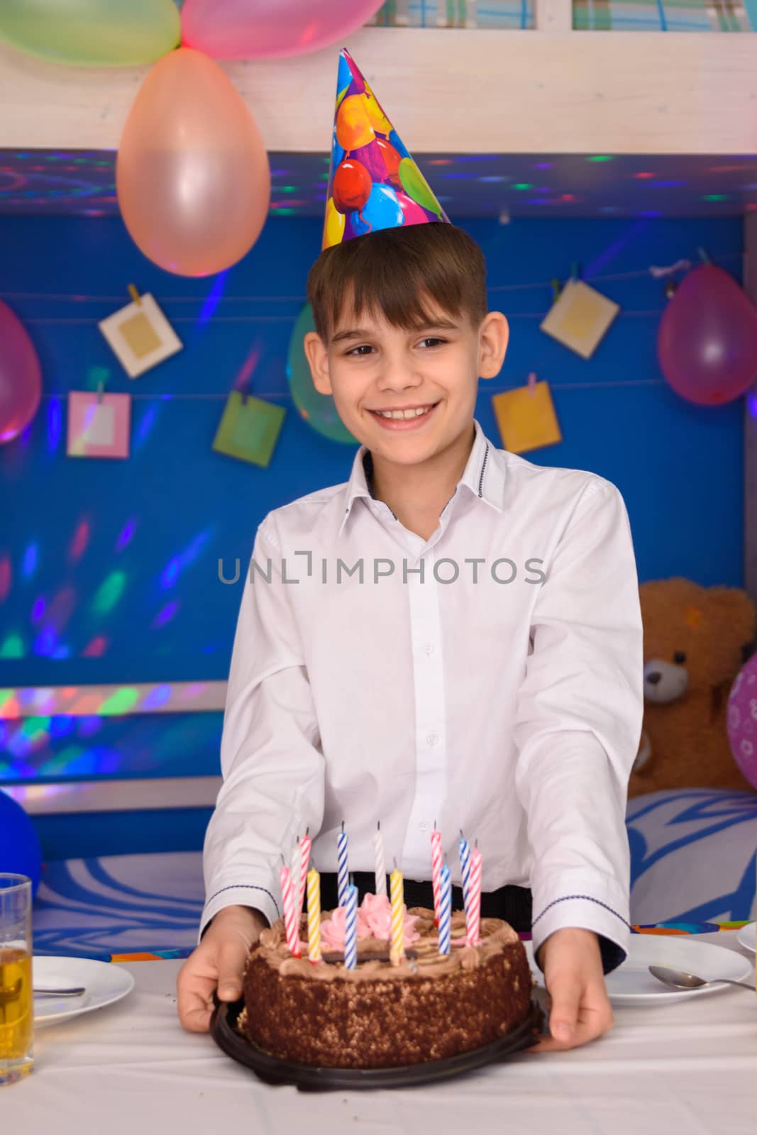 A boy at his birthday stands at the table with a cake