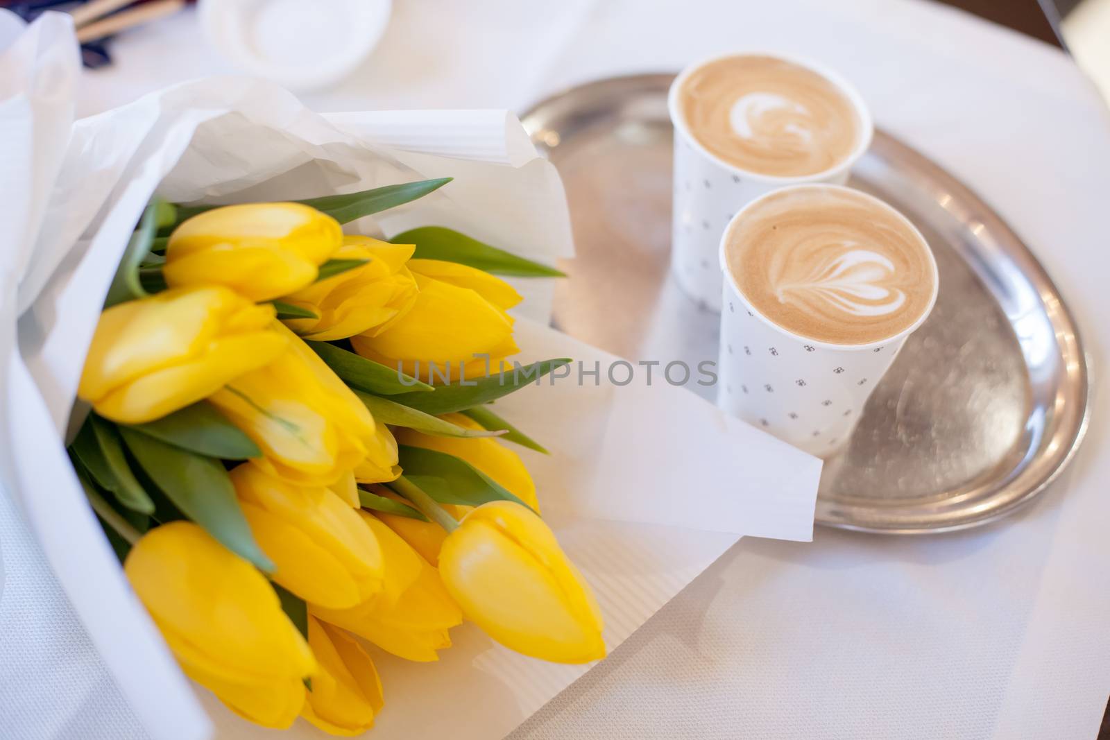 Yellow tulips bouquet with coffee cups over wooden table