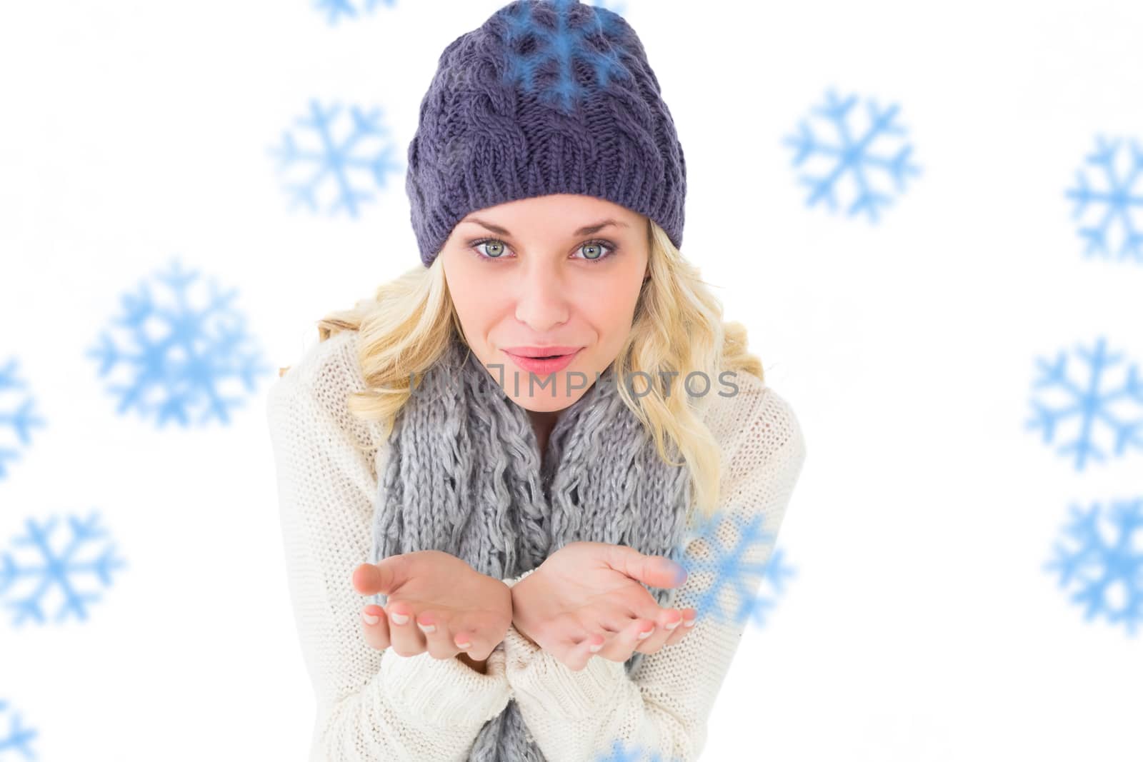 Pretty blonde in winter fashion blowing over hands against snowflakes