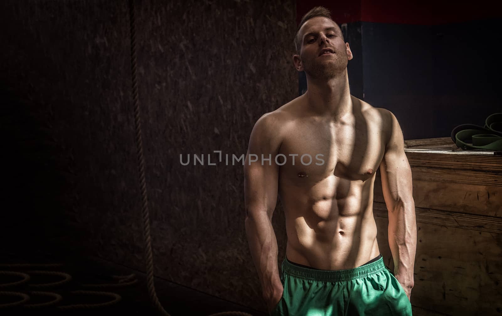 Handsome muscular young man standing in gym during workout, looking at camera