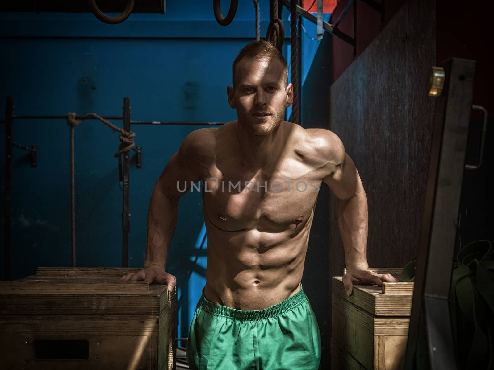 Handsome muscular young man standing in gym during workout, looking at camera